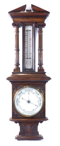 A late 19th/early 20thC aneroid barometer, in a carved oak case, decorated with leaves, fluted columns and a broken pediment, 96cm high.