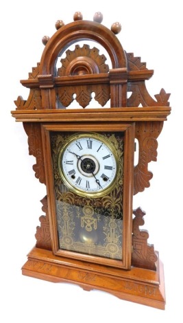 A late 19thC American mantel clock, in gingerbread style walnut case, with pierced crest, above a gilt verre eglomise door, the dial stamped Manufactured By The Ingraham Company Bristol Connecticut, on a plinth, 59cm high.