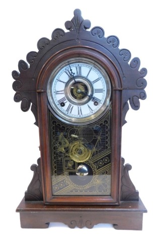 A late 19thC American kitchen or mantel clock, in walnut gingerbread style case, decorated with scrolls etc., with an associated paper dial and alarm etc., enclosed by a gilt Aesthetic verre eglomise door, 52cm high.