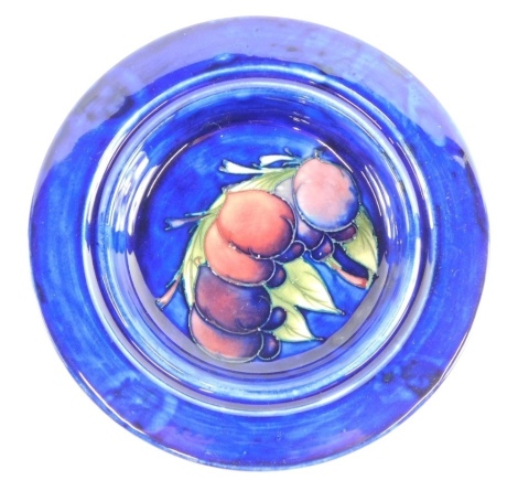 A Moorcroft pottery Plum pattern dish, of circular form, on blue ground, impressed marks beneath, 23cm diameter.