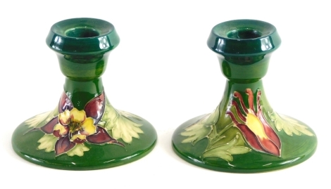 A pair of Moorcroft floral pattern squat candlesticks, on green ground, impressed marks and signature marks beneath, 10cm high.