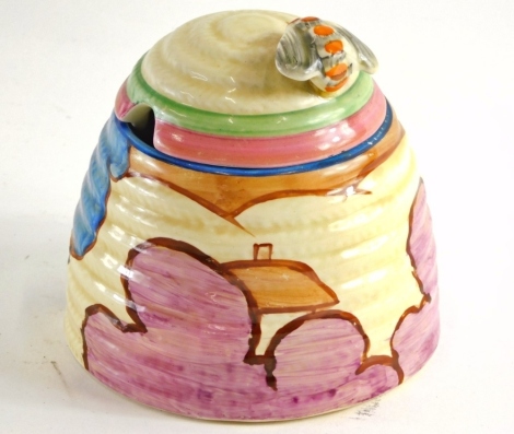 A Clarice Cliff Fantasque Bizarre beehive honey pot, decorated with houses and trees with bee knop, ribbed lid and body, printed marks beneath, 12cm high.