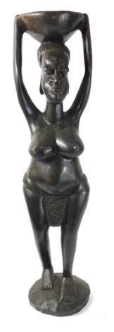 An African carved tribal figure, of a semi clad lady holding bowl to her head on domed base, 66cm high.