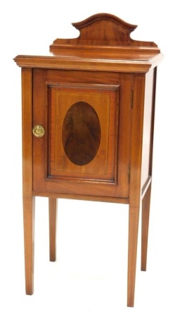 An Edwardian mahogany, boxwood and ebony strung pot cupboard, with a shaped raised back above a panelled door, inlaid with a central oval on square tapering legs, 92cm high, 41cm wide.