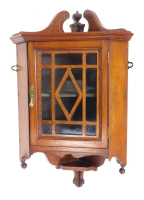 A small Edwardian walnut corner cupboard, the swan neck pediment with central turned finial, above a glazed door with brass drop handle, 71cm high, 44cm diameter.