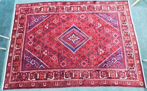 A Persian carpet, with a design of floral lozenges surrounding a central lozenge in navy blue and predominately red, one wide and four narrow borders, 600cm x 283cm.