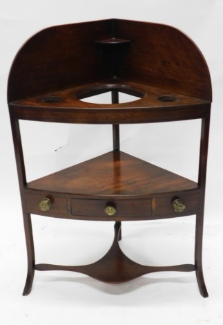 A George III mahogany and ebony strung corner wash stand, with a raised back above three recesses, the undertier with a single drawer flanked by further false drawers, on played legs, 102cm high, 70cm wide.