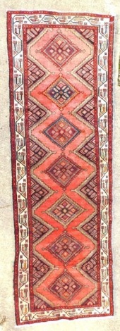 A pink/red ground Persian runner, with a design of medallions, one wide two narrow borders, 174cm x 93cm.