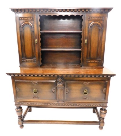 An oak dresser, the top with a dentil cornice above two carved panelled doors flanking two plate shelves, the base with an arrangement of two raised panelled doors flanking a central tapering female caryatid, on cup and cover turned supports and stretcher