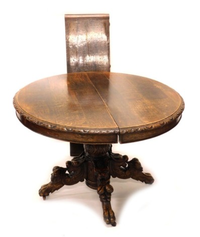 A Victorian oak extending dining table, the circular top with a carved border and one loose leaf, on a leaf carved column and four shaped legs on paw feet, 72cm high, the top 100cm wide when closed.