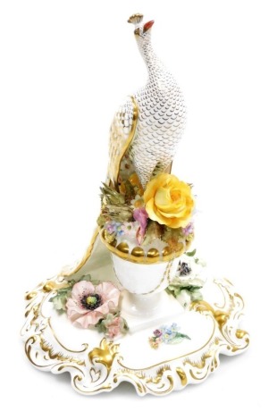 A Royal Crown Derby porcelain model of a peacock, modelled on a floral encrusted urn, on a scroll and floral decorated base, gilt heightened, printed marks and signed to underside K J Fowler and J G Plant, 24.5cm high.