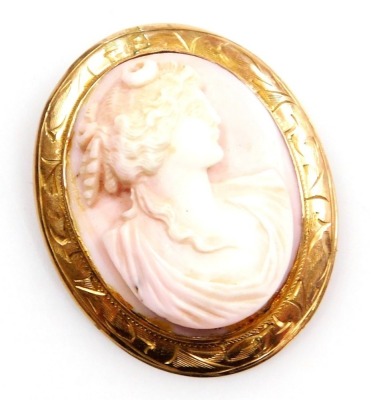 A 20thC pink coral cameo brooch, bust portrait of classical lady, in an oval yellow metal frame, foliate engraved, with safety chain and pin as fitted, 11.7g all in.