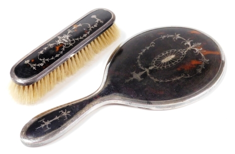 A George V tortoiseshell and silver mounted part dressing table set, with pique decoration, comprising hand mirror and clothes brush, Birmingham 1922. (2)