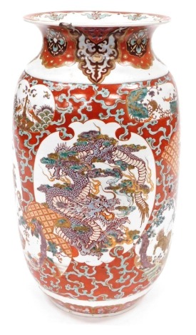 A Japanese Meiji period pottery vase, of cylindrical form with a flared rim, decorated with a reserve to front and verso of a three clawed dragon in clouds, further reserves of birds, trees, etc., on a red ground, 59cm high. (AF)