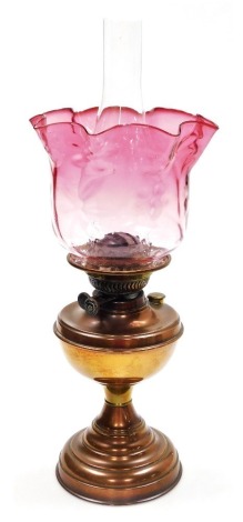 An early 20thC oil lamp, with a graduated pink clear glass shade and a brass central reservoir, on a brass tapering foot, 51cm high.