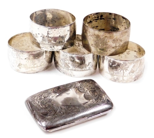 A George V silver cigarette case, with engraved foliate decoration, vacant shield reserve, Birmingham 1917, 1.45oz, together with five Egyptian napkin rings, engraved with a dhow on a river with palm trees beyond, four boxed, one separate. (6)