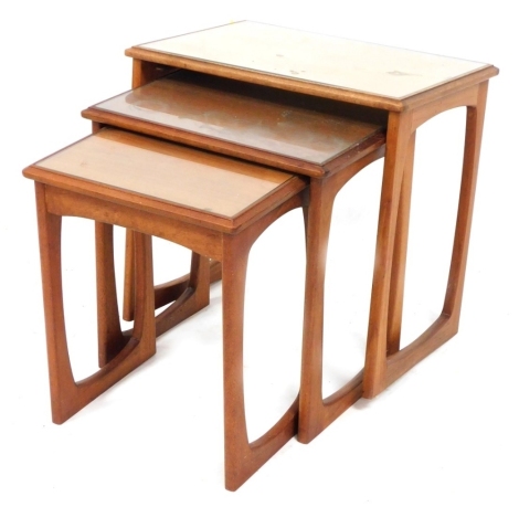 A nest of 1960's teak occasional tables, each with an inset glass top, on open supports to each end, the largest 52cm high, 53cm wide, 37cm deep.