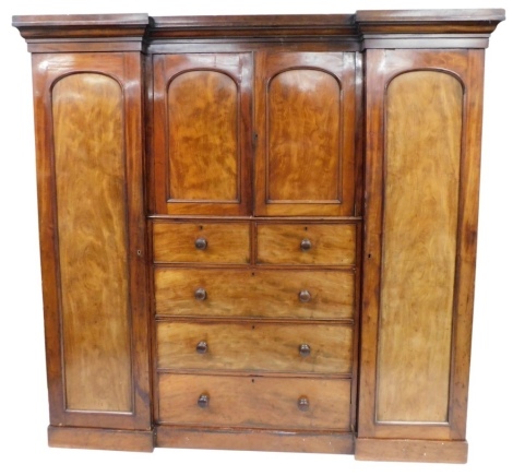 A Victorian mahogany compactum wardrobe, the top with a moulded cornice, the central section with two panelled doors enclosing a fitted shelf, above two short and three long drawers, each side flanked by a single wardrobe, on a plinth base, 202cm high, 11