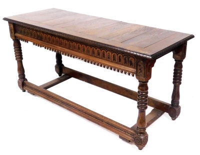 An oak side table, in 17thC style, with a panelled top above a carved edge, the front with carved arched panel, on turned and carved supports, united by a carved stretcher to the front, 72cm high, 157cm wide, 57cm deep.