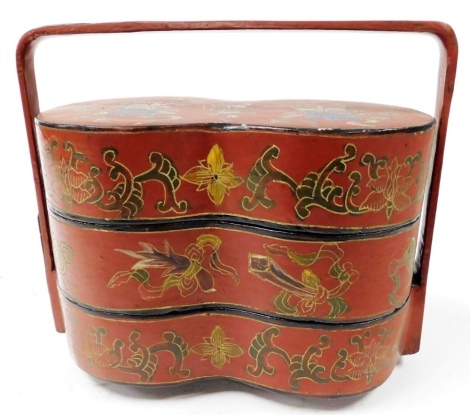 A Chinese three tier red lacquered tiffin box, with strap handle, the exterior painted with scrolling foliage and shrubs, raised on peg feet, 19cm high.