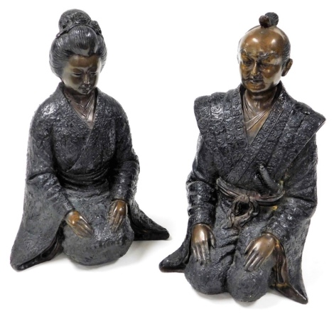 A pair of Oriental bronze patinated cast metal seated figures, of a man with ceremonial robes and daggers, and companion figure of a woman with ceremonial robes and headdress, 30cm and 28cm respectively.