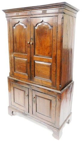 A George III oak livery cupboard, the outswept pediment over a pair of panelled doors opening to reveal two shelves, over two further doors, raised on bracket feet, 183.5cm high, 107cm wide, 50cm deep.