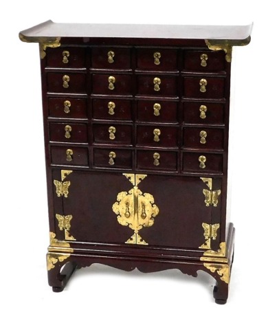 A Korean mahogany apothecary cabinet, with brass mounts, having twenty drawers, above a pair of cupboard doors, raised on bracket feet, 75,5cm high, 59cm wide, 27cm deep.