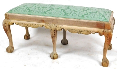 A Georgian style stripped mahogany duet stool, with foliate green upholstered overstuffed seat, above a carved apron, raised on six leaf carved cabriole legs, on ball and claw feet, 104cm wide.