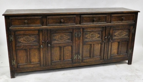 An early 20thC oak sideboard, with four frieze drawers, above four carved panelled doors, raised on stile supports, 84cm high, 180cm wide, 35.5cm deep.