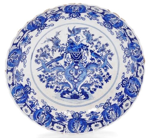 An 18thC Delft blue and white charger, with a waved border, the centre decorated with a vase surrounded by birds and flowers, within a repeating floral border, unmarked, 34.5cm diameter.