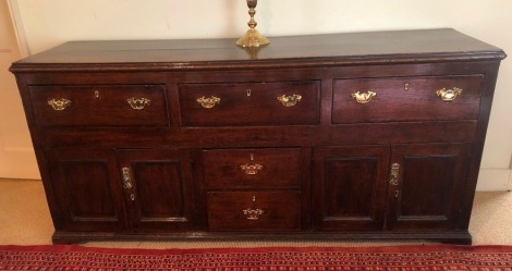 A George III oak dresser base, with moulded top, three drawers over two central drawers, flanked by two panelled doors, all with replacement brass swan neck handles, and bracket feet, 85cm high, 186cm wide, 52cm deep.