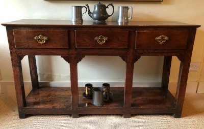 A George II oak dresser base, with single plank top, three frieze drawers with brass swan neck open back plate replacement handles, on plain legs with stiles and pot board, 75cm high, 135cm wide, 39cm deep.