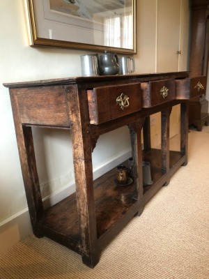 A George II oak dresser base, with single plank top, three frieze drawers with brass swan neck open back plate replacement handles, on plain legs with stiles and pot board, 75cm high, 135cm wide, 39cm deep. - 2