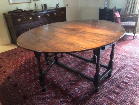 An early 18thC and later tipped gate leg table, with oval top, frieze drawer to each end, turned baluster and block legs, and turned feet raised on later blocks, 72cm high, 135cm wide, 165cm long when extended.