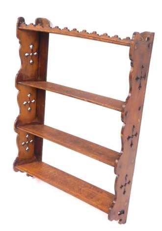 A Victorian Gothic oak wall shelf, with three shelves, supported on shaped ends with carved cross detailing, 86cm high, 63cm wide, 16cm deep.