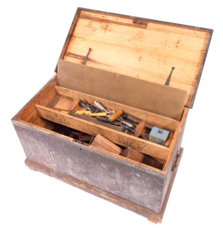 A stained pine carpenter's tool chest, containing moulding planes, braces, saws and other tools, chest 46cm high, 87cm wide, 46cm deep.