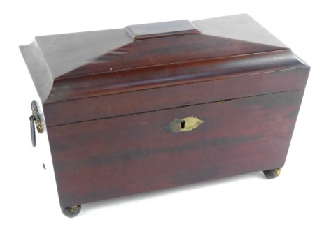 A Regency mahogany sarcophagus shaped tea caddy, with ring handles, the hinged lid opening to reveal a mixing bowl recess, flanked by canisters, raised on brass ball feet, 20cm high, 31cm wide, 15.5cm deep.