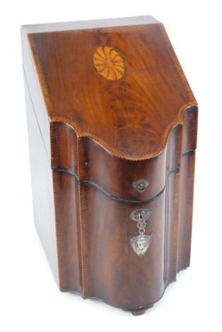 A George III mahogany and satinwood cross banded knife box, of serpentine form, with paterae inlay, and silver escutcheons, one of shield form, crest engraved, the hinged lid opening to reveal a fitted interior, 38cm high, 22cm wide, 29cm deep.