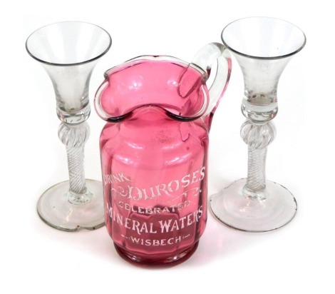 A Victorian cranberry glass water jug, advertising 'Drink Durose's Celebrated Mineral Waters Wisbech', together with a pair of 18thC wine glasses, the trumpet shaped bowl raised above a stem with upper knop, with spiral twist inclusions, raised on a conic