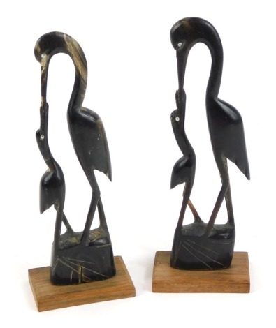 A pair of carved horn sculptures modelled as a stork feeding its young, raised on rectangular wooden base, 22cm high.