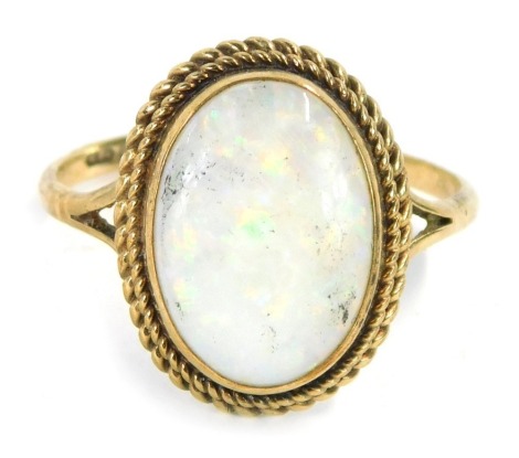 A 9ct gold opal dress ring, the oval opal in a rub over setting, with two row twist border, on V splayed shoulders, ring size S, 3.2g all in.