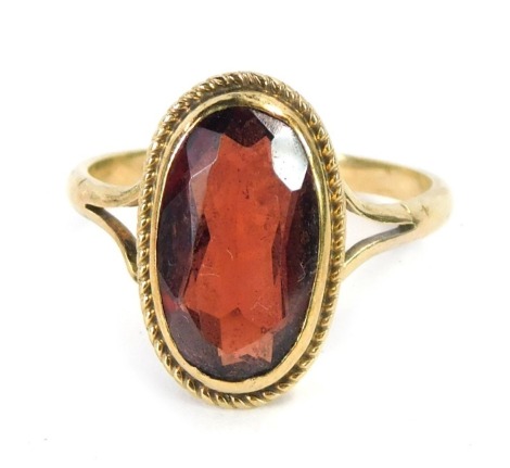 A 9ct gold garnet dress ring, the oval garnet in a rub over setting with rope twist border, on V splayed shoulders, ring size H½, 2g all in.