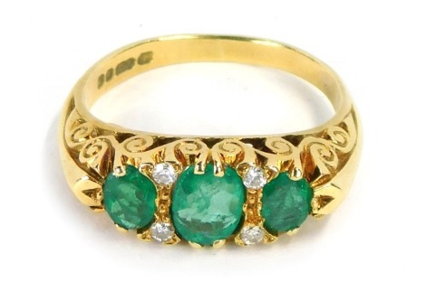 An 18ct gold emerald and diamond gypsy ring, set with three oval cut emeralds and four tiny diamonds, in a scroll outer border, ring size L½, 5.3g all in, boxed.