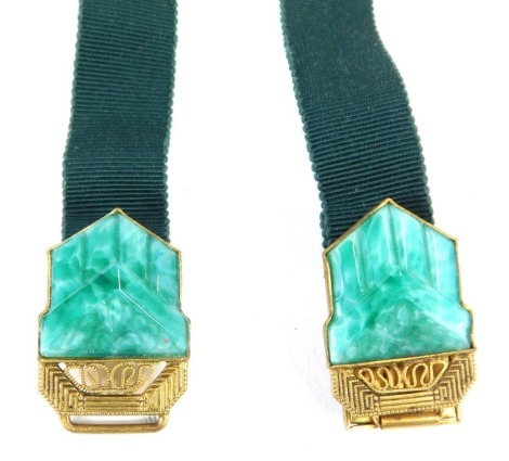 An Art Deco style belt buckle, with two clip clasp set with malachite coloured plastic, on a green ribbon.