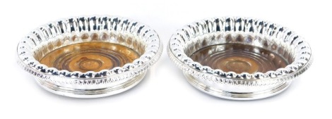 A pair of silver plated wine bottle coasters, each with a fluted rim on ebony base with green baize lining, 15cm diameter.