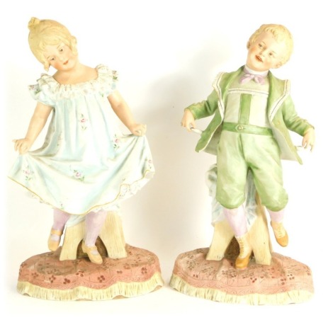 A pair of late 19thC bisque porcelain figures of a girl and boy, in standing pose, on a naturalistic oval carpet base, 36cm and 39cm high respectively.