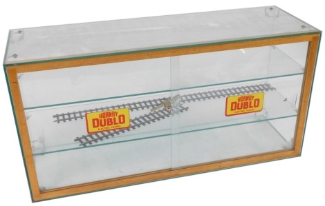 A teak and glass display cabinet, with two glass sliding doors enclosing two glass shelves, the doors bearing stickers for Hornby OO Electric Trains, 46cm high, 91cm wide, 31cm deep.