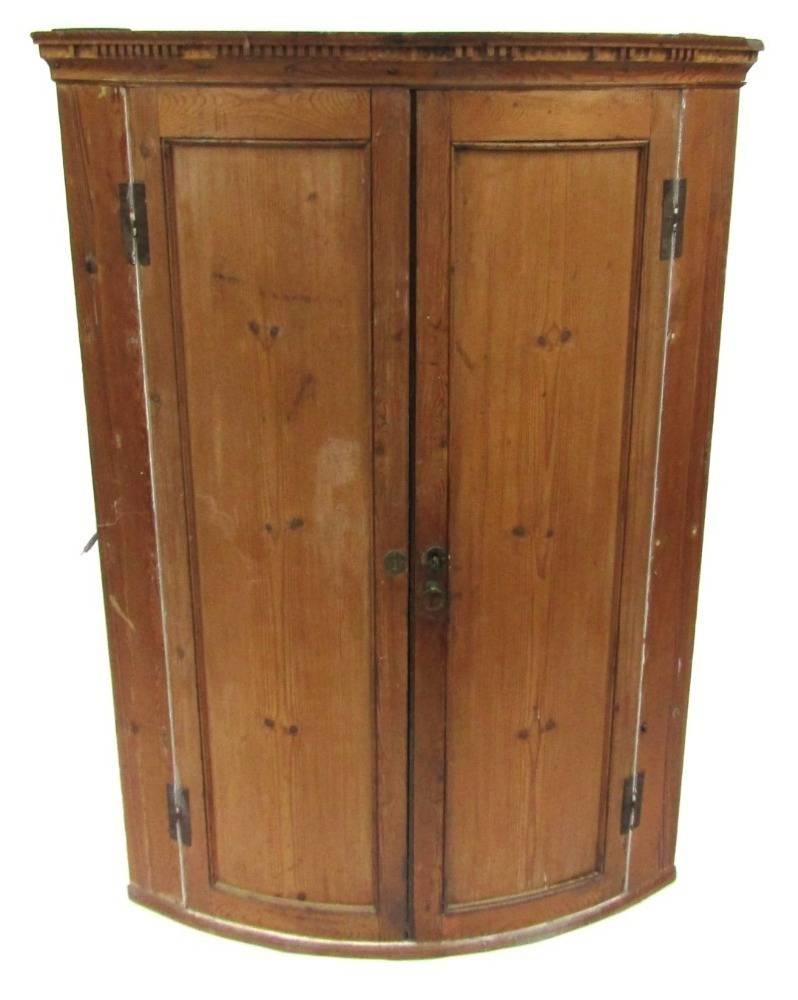 A pine corner cupboard, with a banded top above two curved