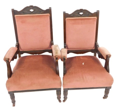 Two Victorian ladies and gents armchairs, each with mahogany frame and pink upholstered seats, with shaped legs terminating in castors.