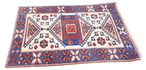 A Middle Eastern rug, on a cream, blue and red ground, with a blue border and central cream panel, with blue and red medallions and tassel ends, 145cm x 102cm.